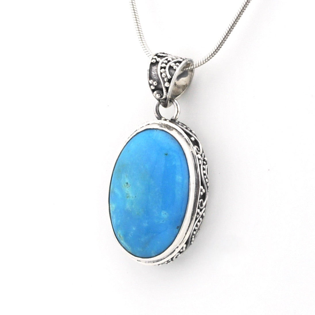 A silver pendant necklace featuring an oval-shaped light blue stone in an ornate silver bezel setting, suspended from a silver snake chain against a plain white background.