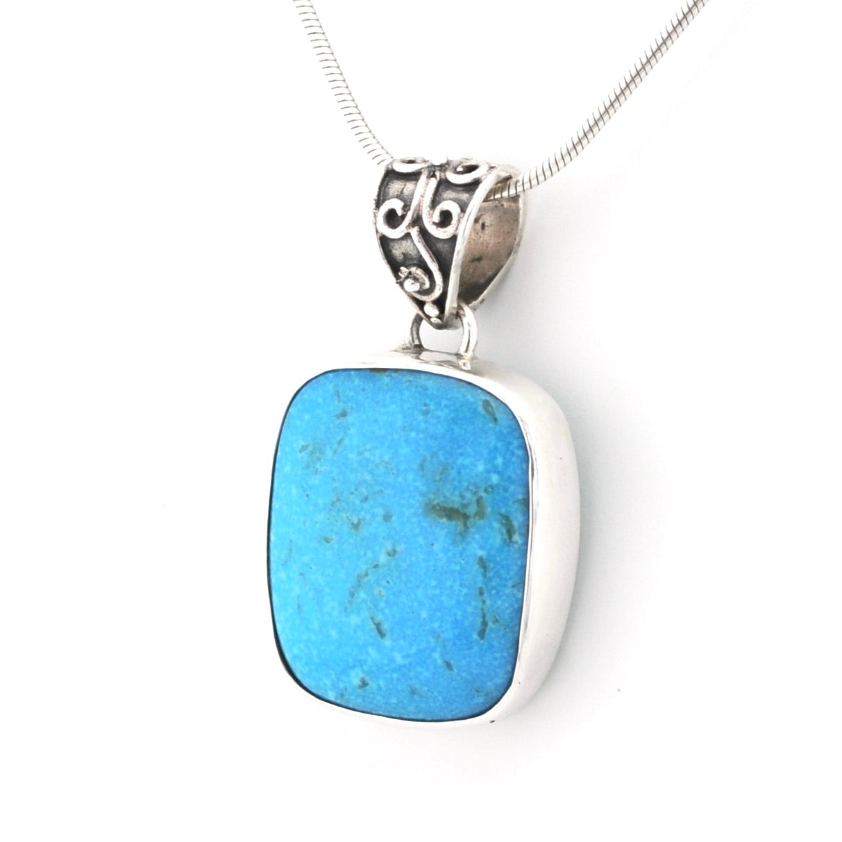 A silver pendant necklace featuring a rectangular turquoise stone with natural green matrix inclusions, set in a polished silver bezel with an ornate silver filigree bail, suspended on a silver snake chain against a white background.