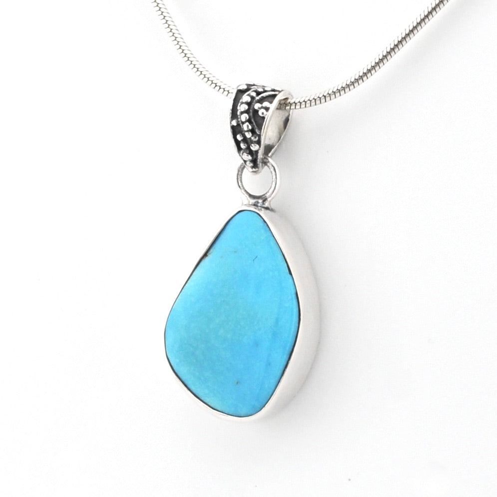 A silver teardrop pendant necklace featuring a smooth, polished turquoise-blue stone in a bezel setting, suspended from a silver snake chain on a white background.