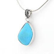 A silver teardrop pendant necklace featuring a smooth, polished turquoise-blue stone in a bezel setting, suspended from a silver snake chain on a white background.