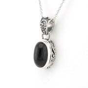 A silver pendant necklace featuring a polished black oval stone set in an ornate silver bezel with scrollwork details, suspended from a silver chain against a plain white background.