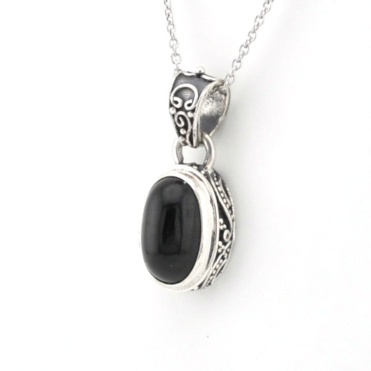 A silver pendant necklace featuring a polished black oval stone set in an ornate silver bezel with scrollwork details, suspended from a silver chain against a plain white background.