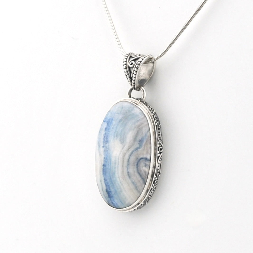 An oval pendant necklace featuring a blue and white marbled stone in a silver-toned bezel setting with an ornate silver chain, shown against a plain white background.