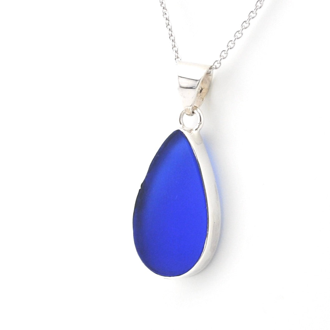 A teardrop-shaped sea glass pendant necklace in vibrant blue with a polished silver bezel and chain, shown on a clean white background.