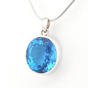 A round-cut blue gemstone pendant in a silver bezel setting on a silver snake chain, photographed against a plain white background.