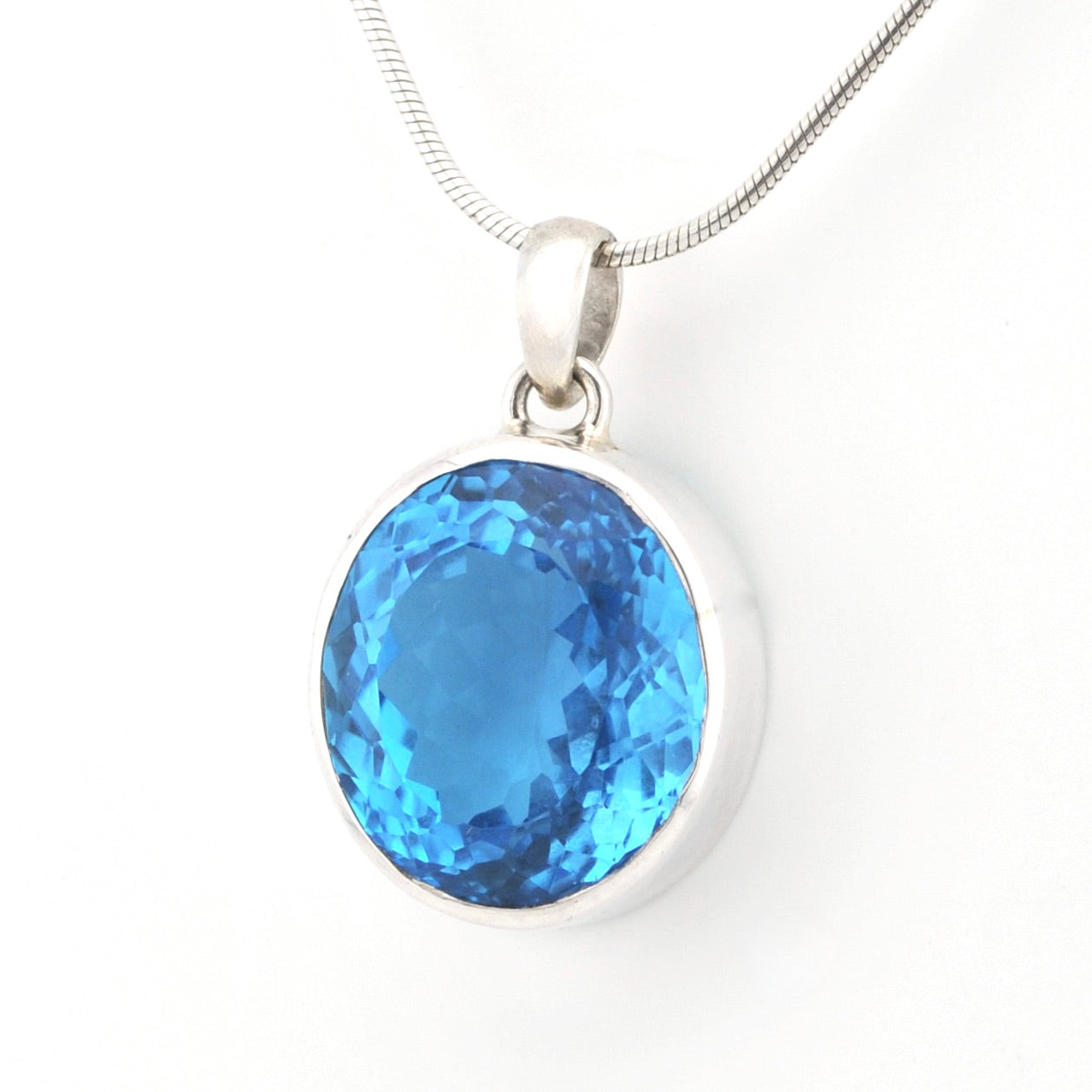 A round-cut blue gemstone pendant in a silver bezel setting on a silver snake chain, photographed against a plain white background.
