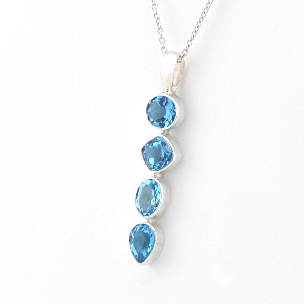 A silver pendant necklace featuring four cascading blue gemstones in different shapes, set against a plain white background.