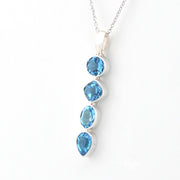 A silver pendant necklace featuring four cascading blue gemstones in different shapes, set against a plain white background.