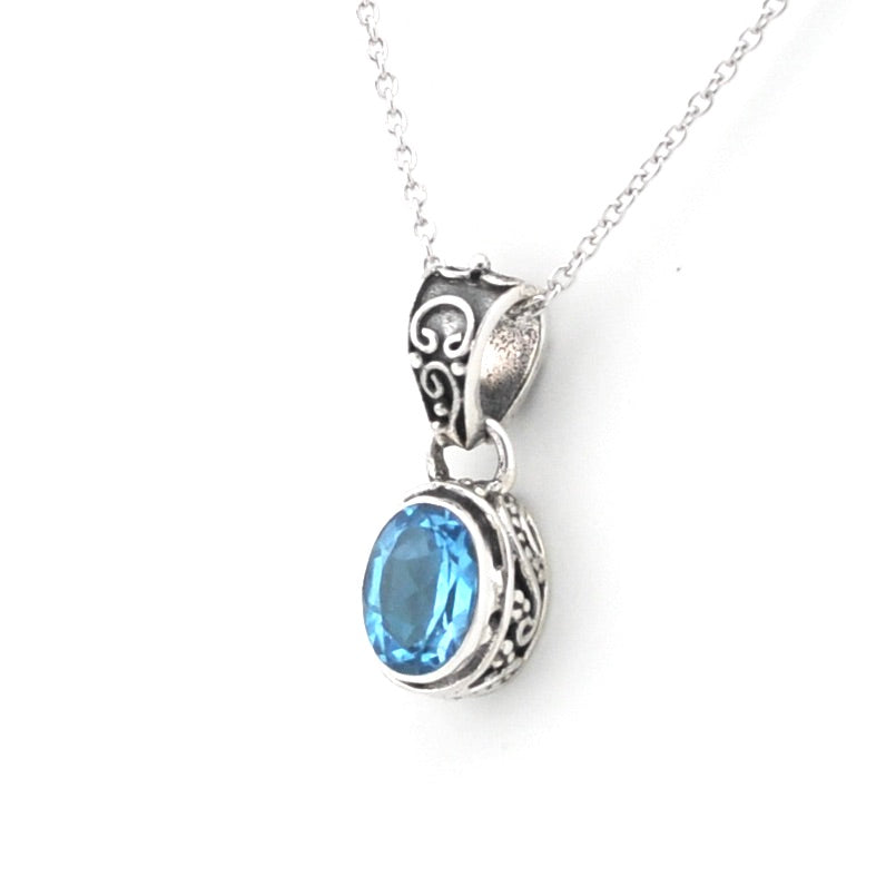 A silver pendant necklace featuring an oval-cut light blue gemstone in an ornate silver bezel setting, suspended from a delicate silver chain against a plain white background.