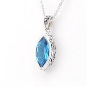 A silver pendant necklace featuring a marquise-cut blue gemstone in an ornate silver bezel setting, suspended from a delicate silver chain against a plain white background.