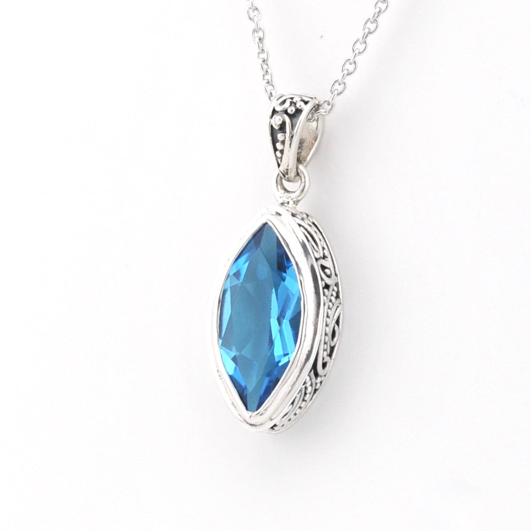 A silver pendant necklace featuring a marquise-cut blue gemstone in an ornate silver bezel setting, suspended from a delicate silver chain against a plain white background.
