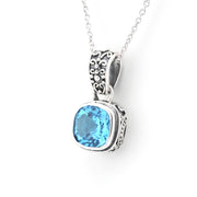A silver pendant necklace featuring a cushion-cut light blue gemstone in an ornate, textured silver bezel setting, suspended from a delicate silver chain against a plain white background.