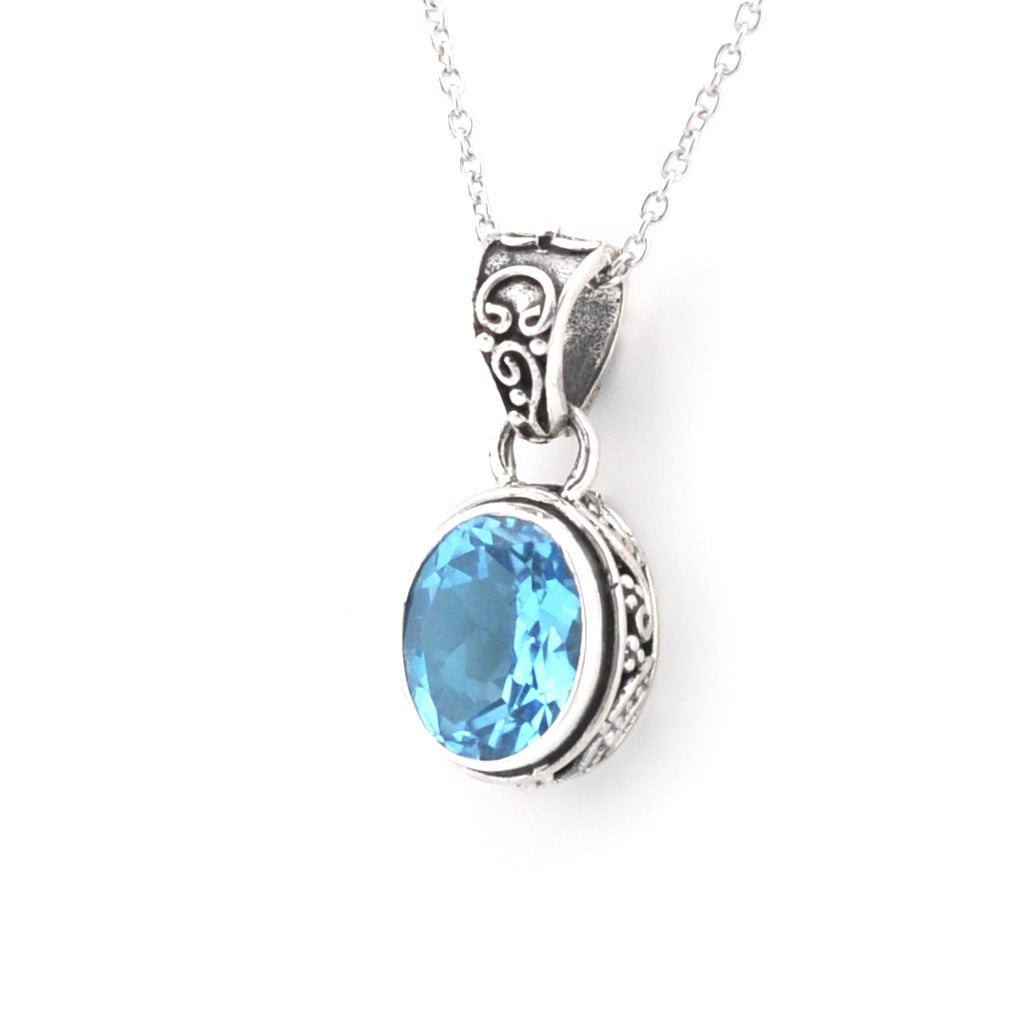 A silver pendant necklace featuring an oval-cut light blue gemstone in an ornate silver bezel setting, suspended from a delicate silver chain against a plain white background.