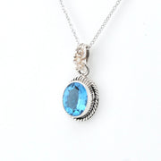A silver pendant necklace featuring an oval-cut light blue gemstone in a textured bezel setting, suspended from a delicate silver chain against a plain white background.