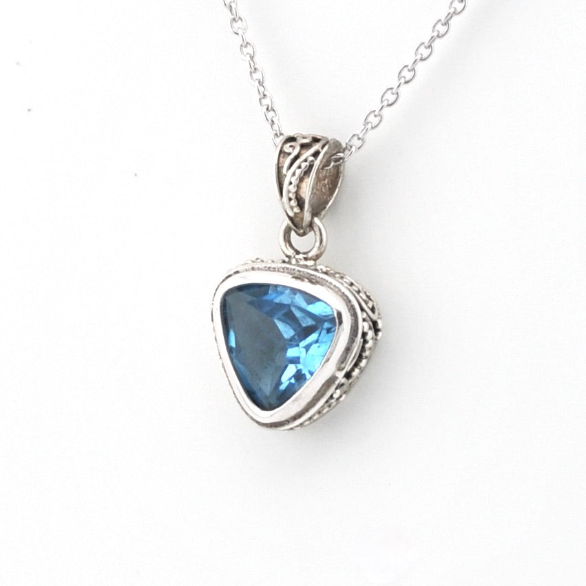 A silver pendant necklace featuring a triangular blue gemstone in a textured silver bezel setting, suspended from a silver chain against a plain white background.