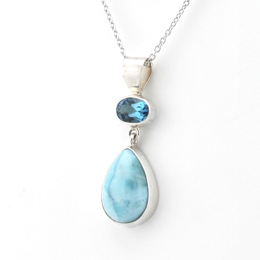 A silver pendant necklace featuring a large teardrop-shaped light blue larimar stone and a smaller oval blue topaz stone, shown on a white background.