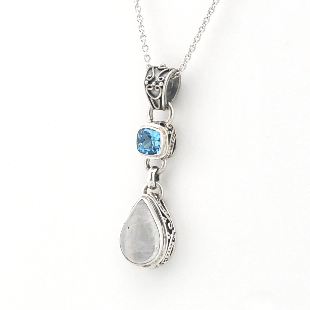 A silver-toned dangle pendant necklace featuring a small square blue gemstone and a larger teardrop-shaped milky white gemstone, suspended from a delicate silver chain against a plain white background.