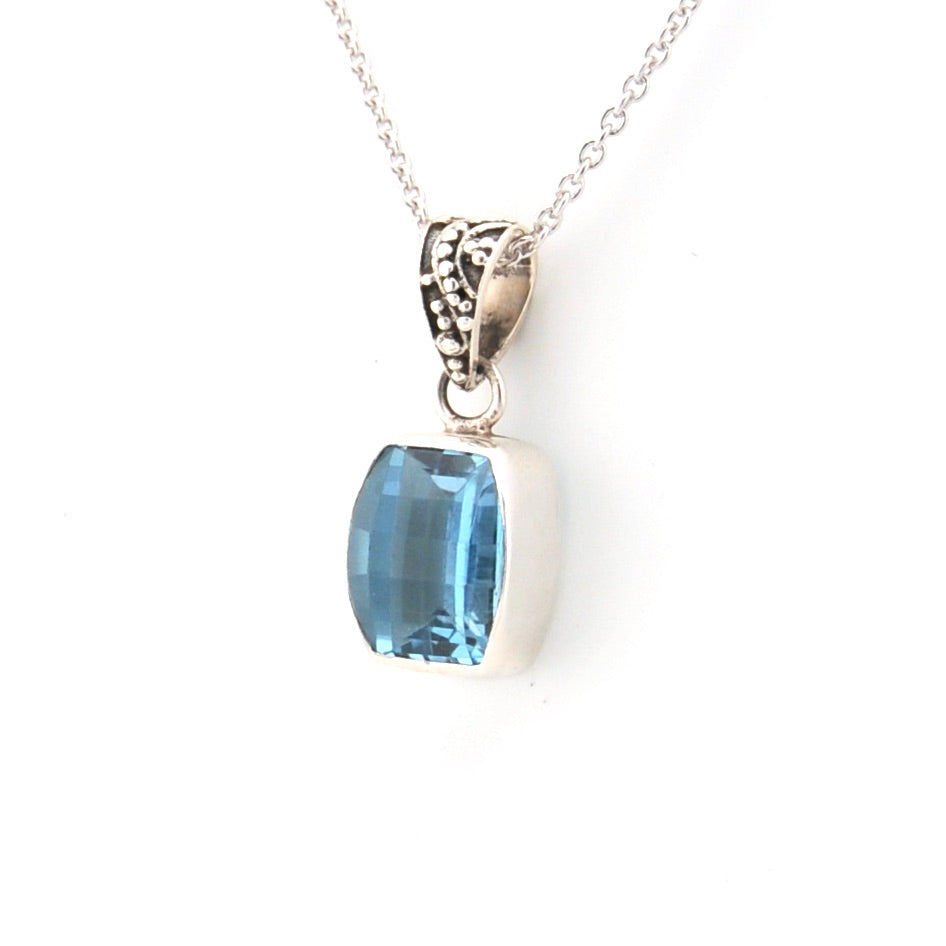 Blue gemstone pendant on a silver chain against a white background