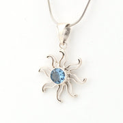 Silver sun-shaped pendant with a blue gemstone on a white background