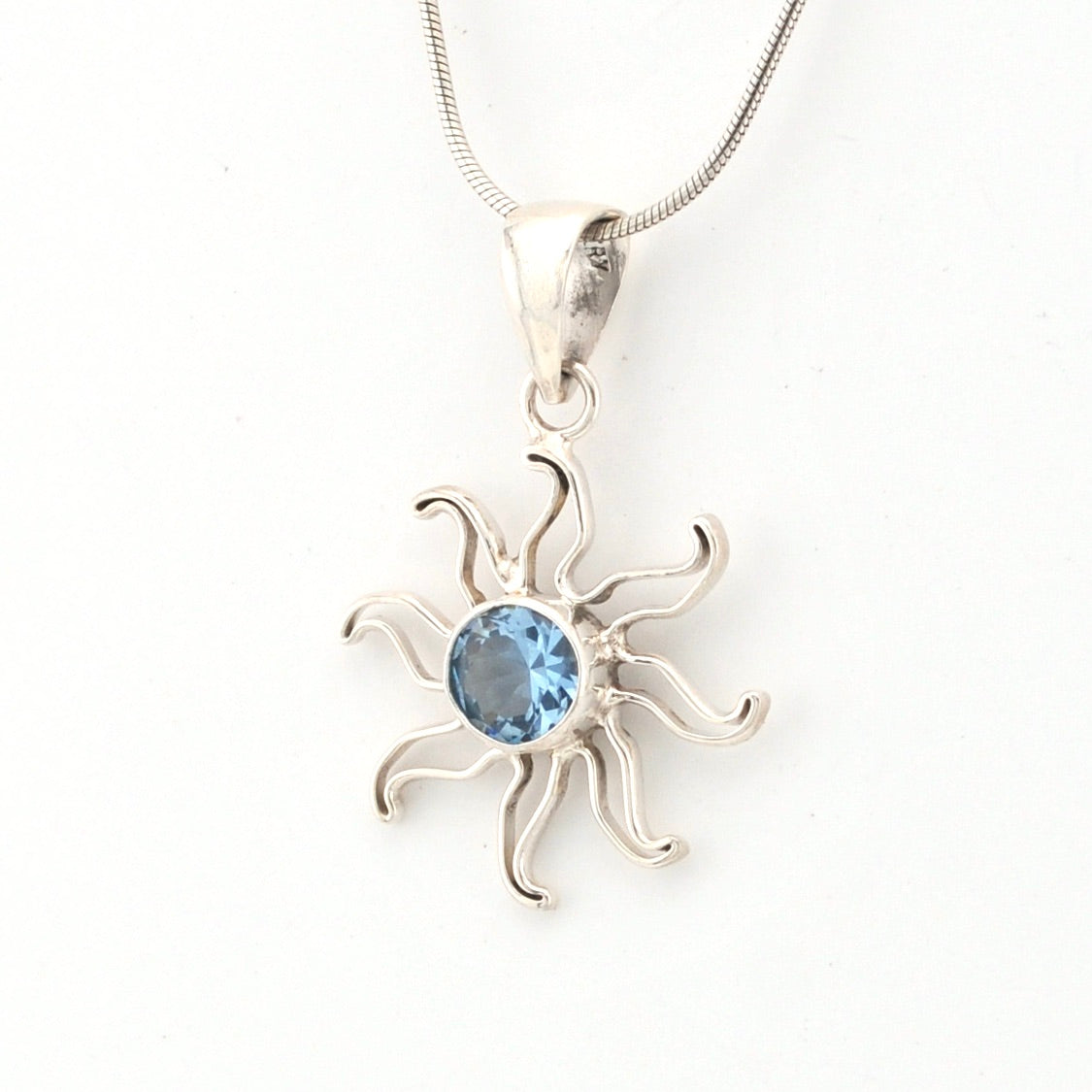 Silver sun-shaped pendant with a blue gemstone on a white background