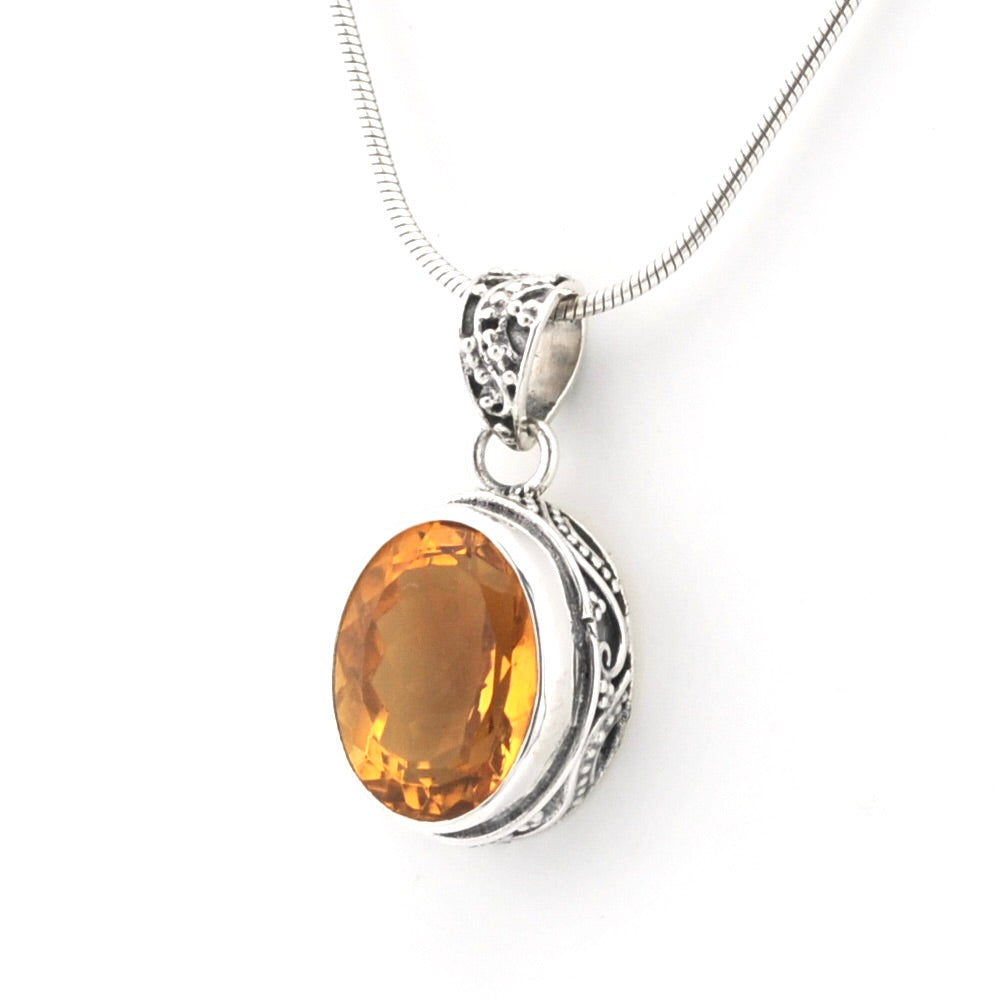 An oval amber gemstone pendant in a silver-toned filigree bezel setting, suspended from a silver snake chain against a plain white background.