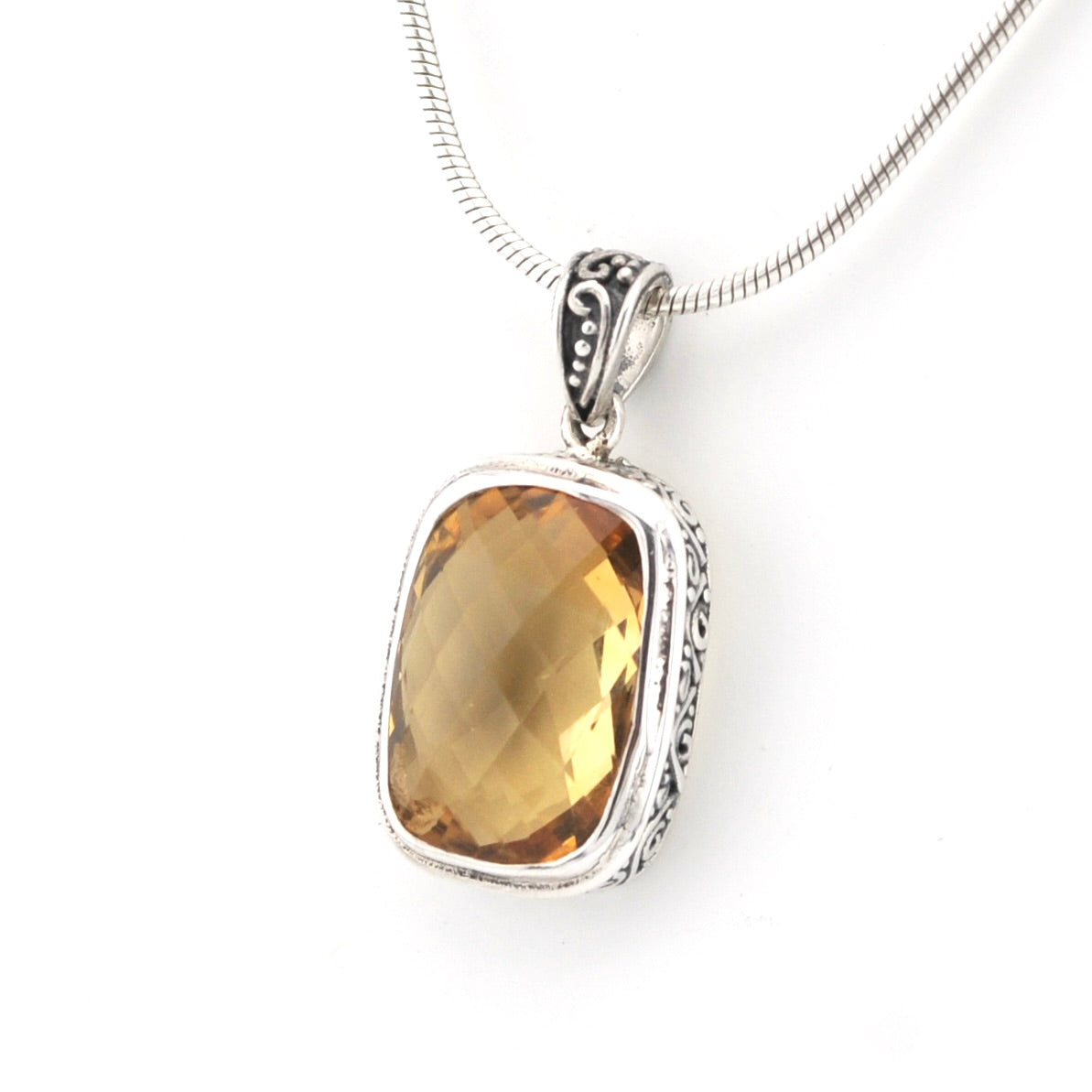 A silver pendant necklace featuring a large, cushion-cut faceted amber citrine gemstone in a silver bezel setting, suspended from a silver snake chain against a plain white background.