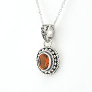 An oval pendant necklace featuring a faceted orange gemstone in a textured silver bezel with a twisted rope border, suspended from a delicate silver chain against a plain white background.