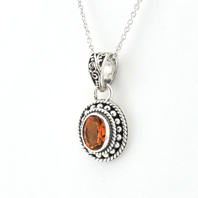 An oval pendant necklace featuring a faceted orange gemstone in a textured silver bezel with a twisted rope border, suspended from a delicate silver chain against a plain white background.
