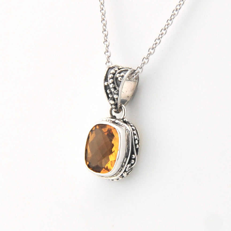 Silver pendant with a yellow gemstone on a white background