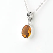 An oval-cut amber gemstone pendant set in a silver bezel with a silver chain, shown against a plain white background.