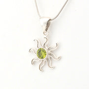 Silver sun-shaped pendant with a green gemstone on a white background