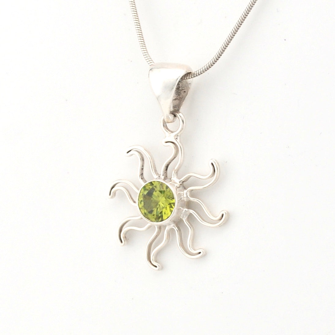 Silver sun-shaped pendant with a green gemstone on a white background