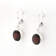A pair of silver leverback drop earrings featuring oval dark reddish-brown gemstone charms, displayed on a clean white background.