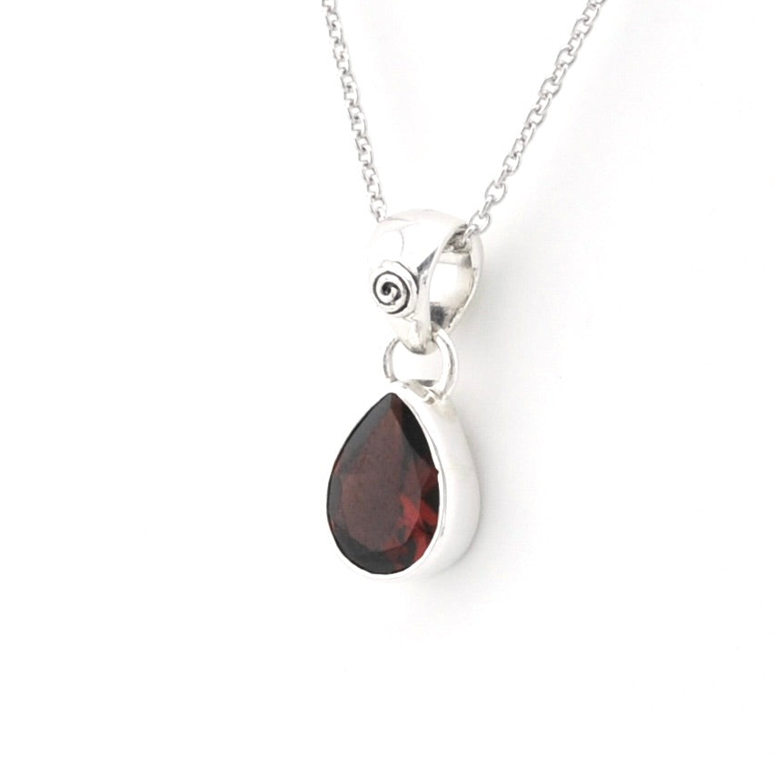 A silver pendant necklace featuring a teardrop-shaped dark red gemstone pendant set in a polished silver bezel, suspended from a delicate silver chain against a plain white background.