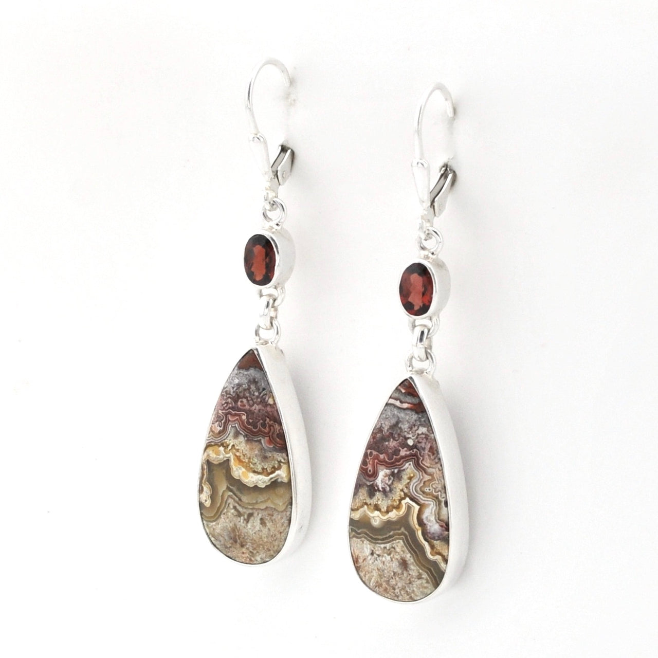 A pair of teardrop dangle earrings featuring natural agate geode patterns in silver bezel settings with small round garnet accents, shown on a plain white background.