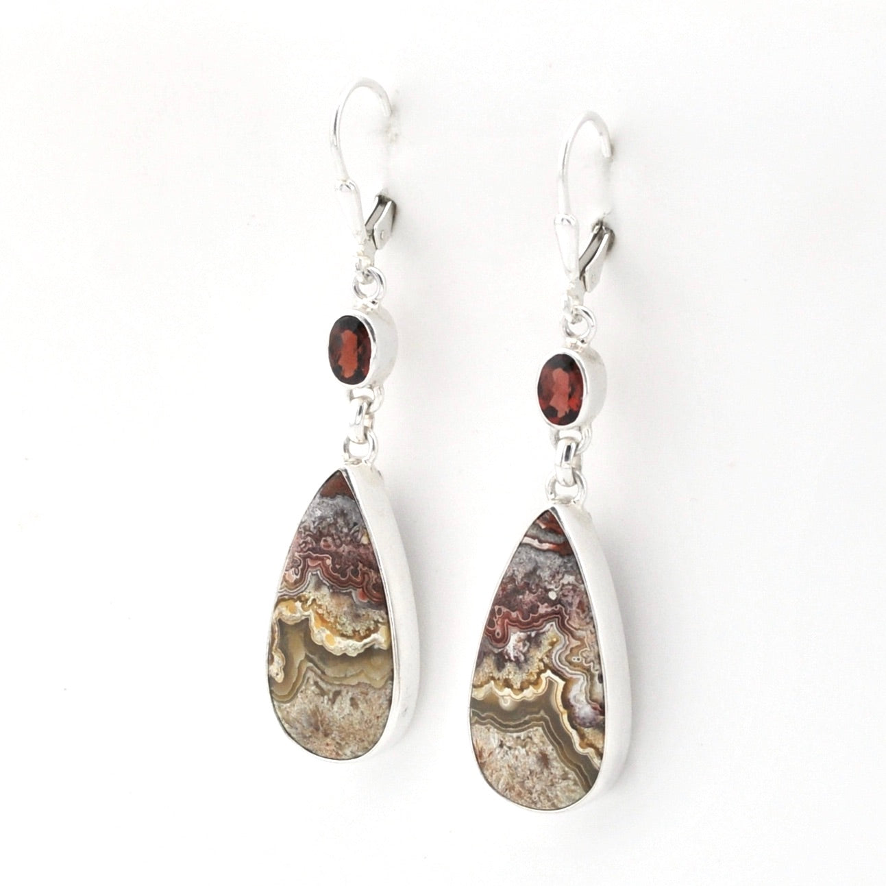 A pair of teardrop dangle earrings featuring natural agate geode patterns in silver bezel settings with small round garnet accents, shown on a plain white background.