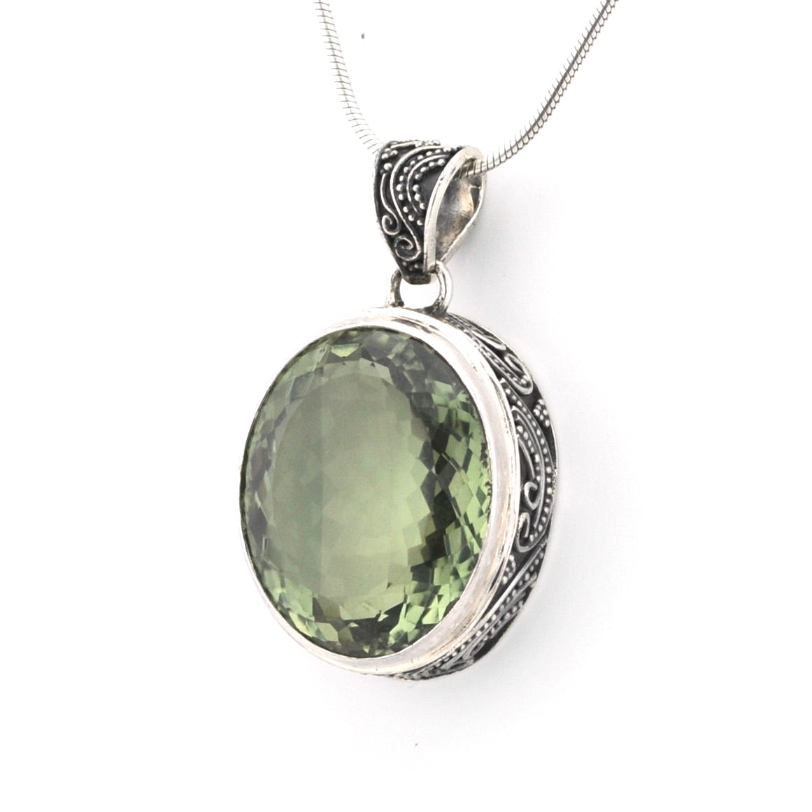 An oval pendant necklace featuring a faceted olive-green gemstone in a silver bezel with ornate filigree detailing on the bail and sides, suspended from a silver chain against a plain white background.