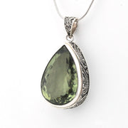 A teardrop-shaped green gemstone pendant in an ornate silver bezel setting with a matching silver chain, shown against a plain white background.