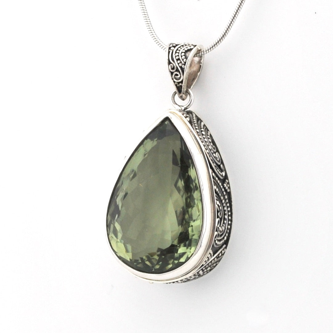 A teardrop-shaped green gemstone pendant in an ornate silver bezel setting with a matching silver chain, shown against a plain white background.