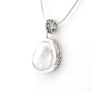 A sterling silver pendant necklace featuring a large, irregular white pearl set in an ornate filigree bezel, suspended from a silver snake chain against a plain white background.