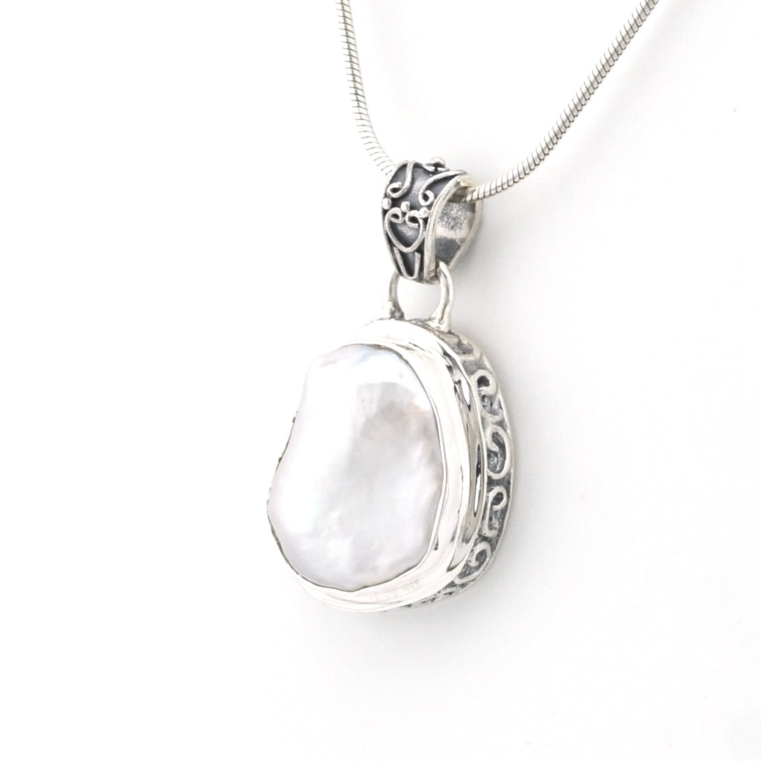 A sterling silver pendant necklace featuring a large, irregular white pearl set in an ornate filigree bezel, suspended from a silver snake chain against a plain white background.