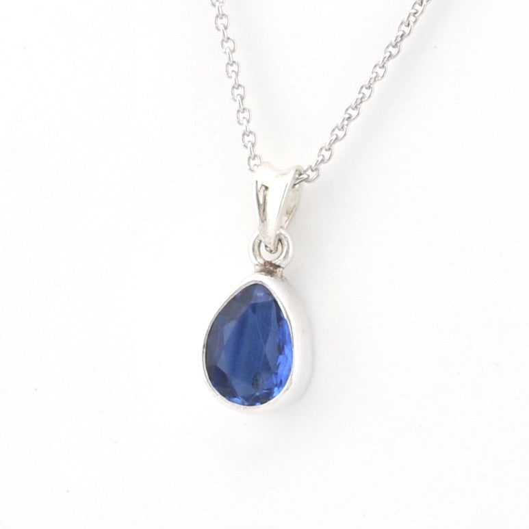 A silver teardrop pendant necklace featuring a faceted blue gemstone, shown on a clean white background.