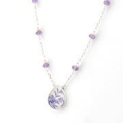A silver chain necklace featuring a teardrop-shaped pendant with a blue floral pattern on a white background, accented by small white pearls and purple beads on a white studio background.