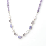 A silver beaded necklace featuring lavender amethyst beads, white pearls, and smooth gray sea glass chips, displayed on a clean white background.