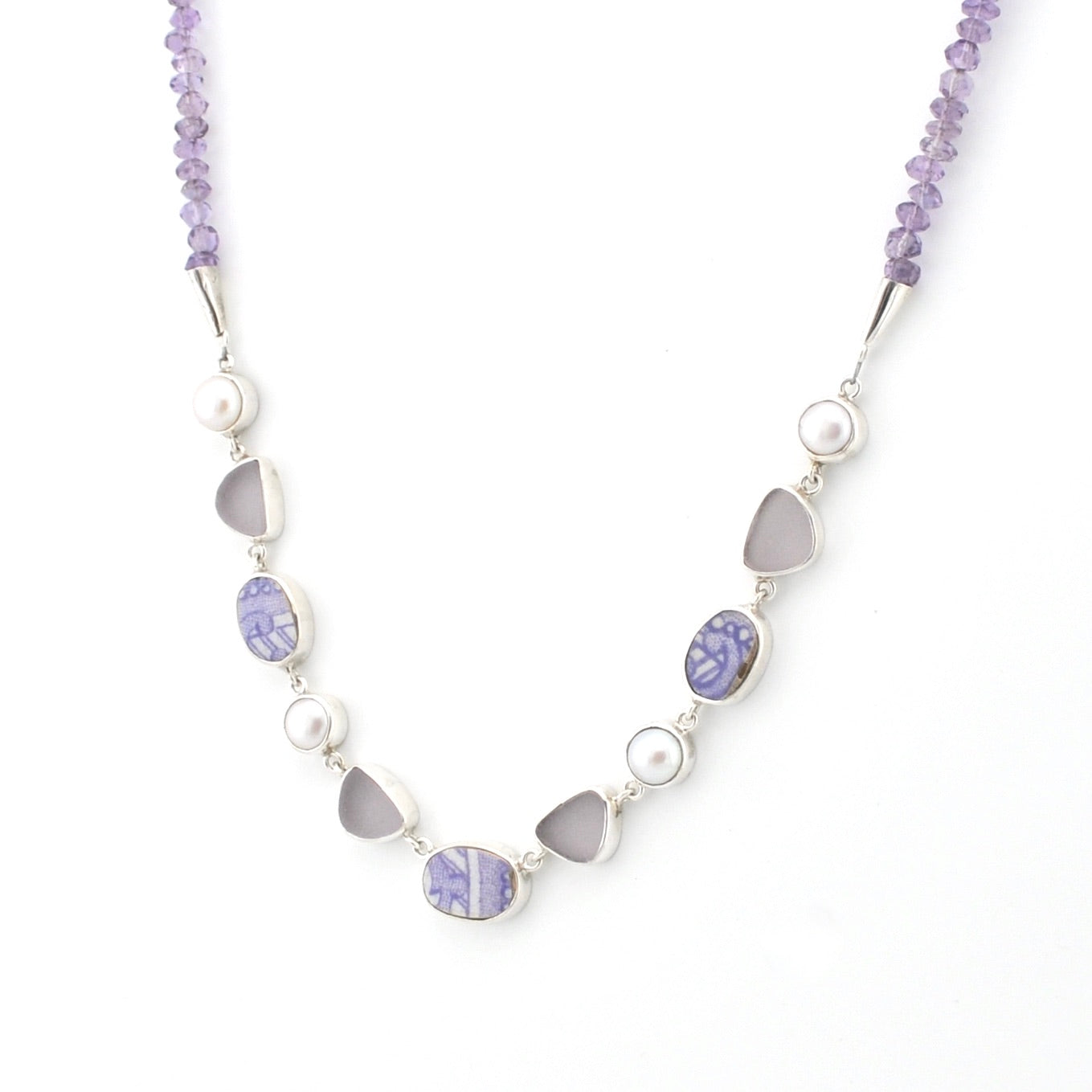 A silver beaded necklace featuring lavender amethyst beads, white pearls, and smooth gray sea glass chips, displayed on a clean white background.