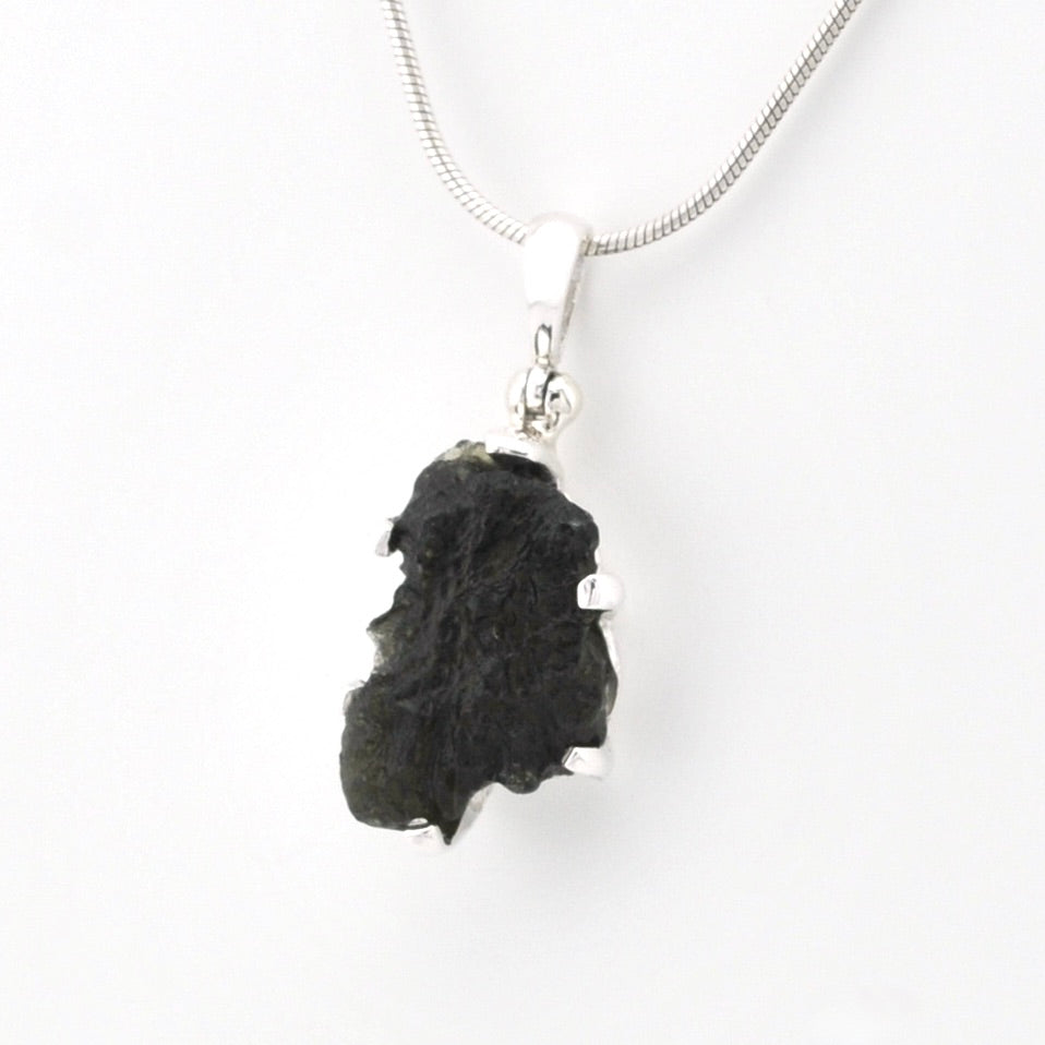 A silver snake chain necklace featuring a raw, irregular black stone pendant, shown against a plain white background.