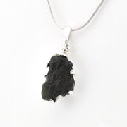 A silver snake chain necklace featuring a raw, irregular black stone pendant, shown against a plain white background.