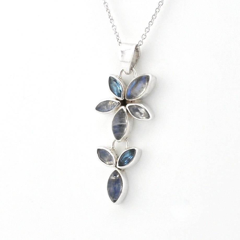 A silver pendant necklace featuring a vertical arrangement of marquise-cut blue and smoky gray gemstones in a floral leaf design, suspended from a delicate silver chain against a plain white background.
