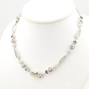 A silver-toned beaded necklace displayed on a white mannequin bust. The necklace features a mix of polished shell, white topaz, small white pearl, and gray stone.