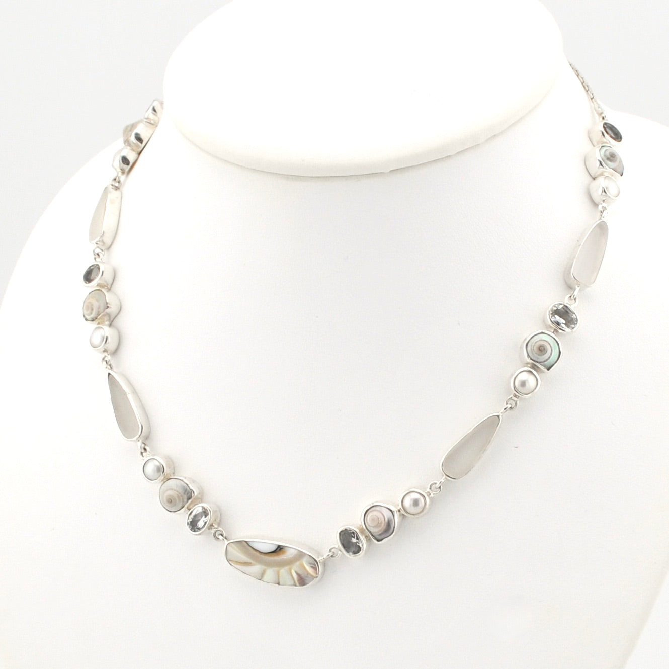 A silver-toned beaded necklace displayed on a white mannequin bust. The necklace features a mix of polished shell, white topaz, small white pearl, and gray stone.